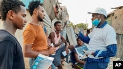 In this photo taken Wednesday, May 20, 2020, stranded Ethiopian migrants receive informational materials informing them how to protect themselves against the coronavirus, in Bosaso, Somalia. (International Organization for Migration (IOM) - Somalia via AP)