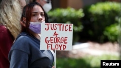 A protester holds a sign outside the Florida home of former Minneapolis Police Officer Derek Chauvin, who has been charged in George Floyd's death, in the Windermere neighborhood of Orlando, Fla., May 29, 2020.