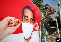 FILE - A worker sits on a ladder as he installs a coronavirus awareness-themed banner bearing a portrait of Indonesian President Joko Widodo wearing a face mask, in Jakarta, Indonesia, Aug. 26, 2020.