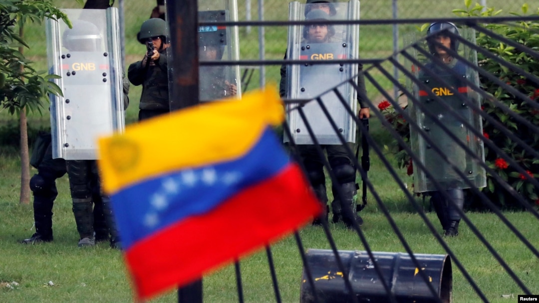 FILE - A member of the riot security forces points a gun at an opposition supporter holding a Venezuelan national flag during clashes at a rally against Venezuelan President Nicolas Maduro's government in Caracas, June 22, 2017. 