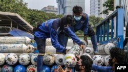 Pekerja menurunkan tangki oksigen di stasiun oksigen darurat di dekat Monas, Jakarta, 5 Juli 2021. (Foto : Mariana/AFP)
