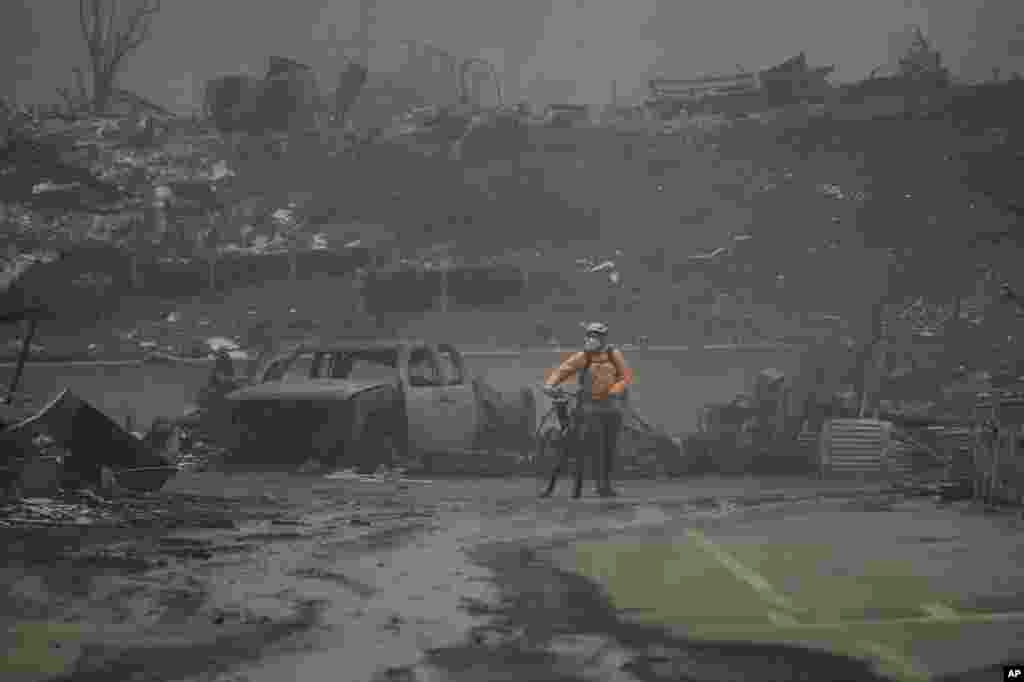 A man walks his bike among the ruins left behind by the Palisades Fire in the Pacific Palisades neighborhood of Los Angeles, California.&nbsp;Multiple massive wildfires are tearing across the Los Angeles area with devastating force. The flames drove residents to make desperate escapes from burning homes through ferocious winds and towering clouds of smoke. At least two people have died and numerous have been injured. (AP Photo/Damian Dovarganes)