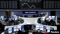 FILE - Traders work at their desks in front of the German share price index, DAX board, at the stock exchange in Frankfurt, Germany, Feb. 19, 2016.