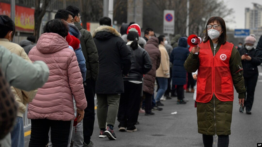 En esta foto publicada por la Agencia de Noticias Xinhua, un voluntario que usa una máscara facial para protegerse del coronavirus usa un altavoz para dar consejos a los residentes enmascarados el 9 de enero de 2022.