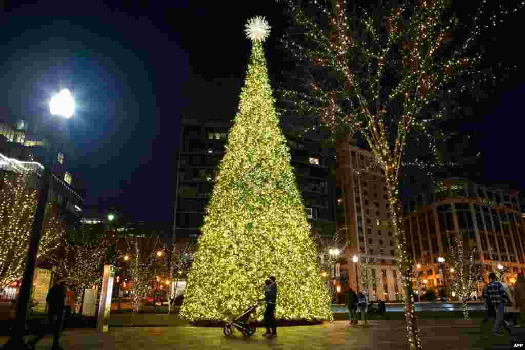 Una pareja y su beb&#233; pasean frente a un &#225;rbol de Navidad en el centro de Washington, D.C., el 12 de diciembre de 2020. Las caminatas nocturnas para ver las decoraciones es algo a lo que muchos no renuncian pese al coronavirus. [AFP]