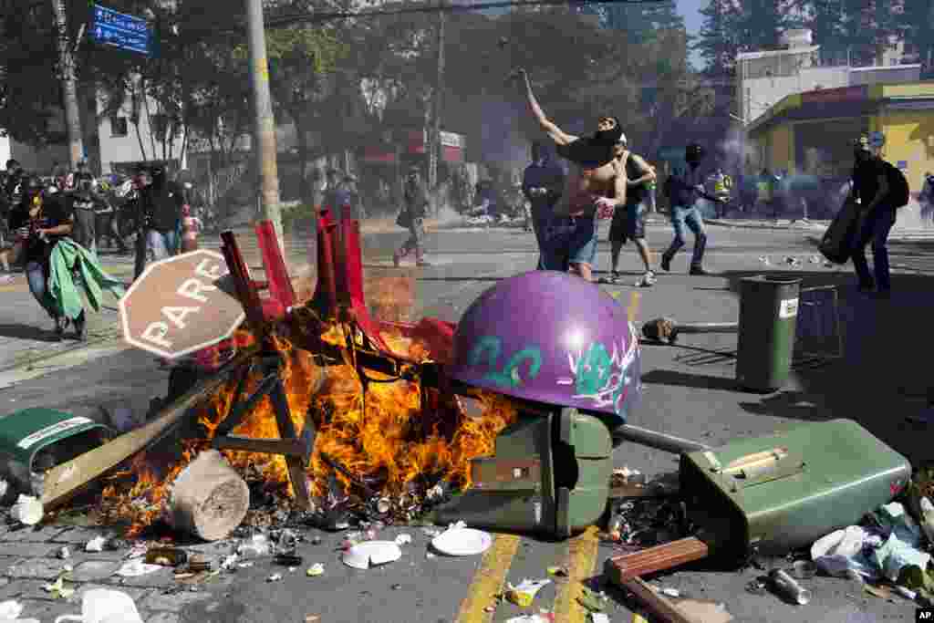 Seorang pria bertopeng melemparkan batu ke arah polisi anti-huru-hara dalam protes yang menuntut perbaikan layanan publik dan melawan uang yang dihabiskan untuk Piala Dunia, di Sao Paulo, Brazil (12/6). (AP/Rodrigo Abd)