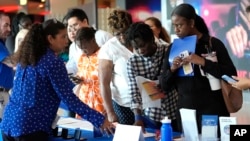 FILE - Carolina Wilson, with the United States Postal Service, left, talks with prospective job applicants at a job fair, Aug. 29, 2024, in Sunrise, Fla.