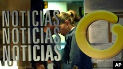 FILE - An employee at Globovision, a 24-hour television news channel, works behind a glass reading "News" with Globovision's logo "G" at the channel's headquarters in Caracas, Venezuela, Oct. 3, 2003.