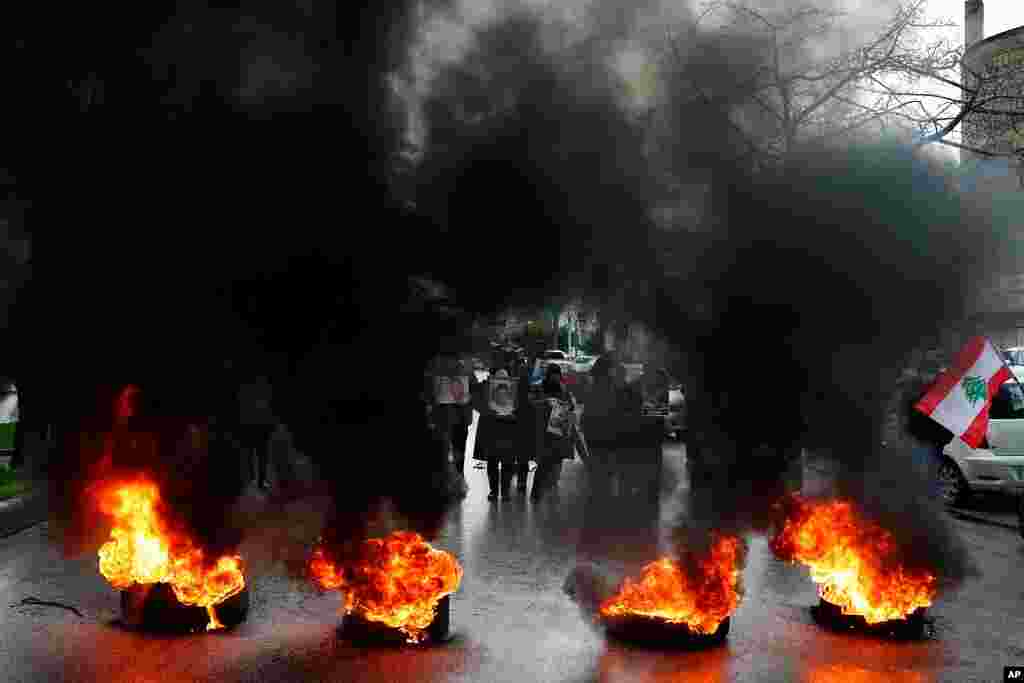 Relatives of victims of the Aug. 4, 2020, Beirut port explosion hold portraits of their loved ones who killed during the explosion, as they burn tires to block a road during a sit-in outside the Justice Palace, in Beirut, Lebanon.