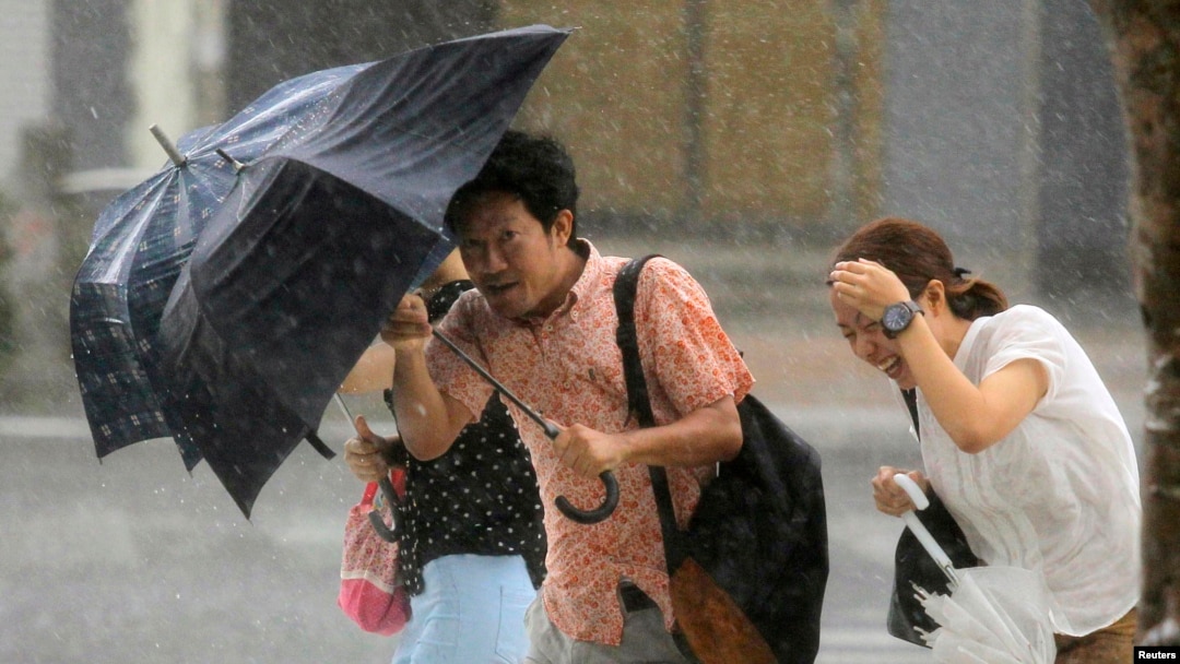 People holding umbrellas walk against strong winds and heavy rain brought by Typhoon Neoguri on a street in Naha, on Japan's southern island of Okinawa, July 9, 2014. 