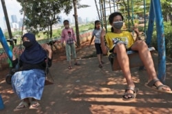 Indonesian children wearing face masks as a precaution against coronavirus outbreak play on swings in Jakarta, Indonesia, Sept. 23, 2020.