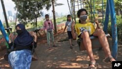 FILE - Indonesian children wearing face masks as a precaution against coronavirus outbreak play on swings in Jakarta, Indonesia, Sept. 23, 2020.