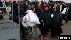 গাজার দক্ষিণাঞ্চলে রাফায় জাতিসংঘের ত্রাণ সংস্থা ইউএনআরডব্লিউএ-র বিতরণ করা ময়দার ব্যাগ পরিবহনের জন্য ফিলিস্তিনিরা হুইলচেয়ার ব্যবহার করছে। ২৯ জানুয়ারি, ২০২৪।