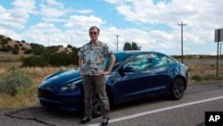 Howard Coe poses in front of his wife's Tesla sedan, Sept. 14, 2021, on a road near Nambé Pueblo outside Santa Fe, N.M.