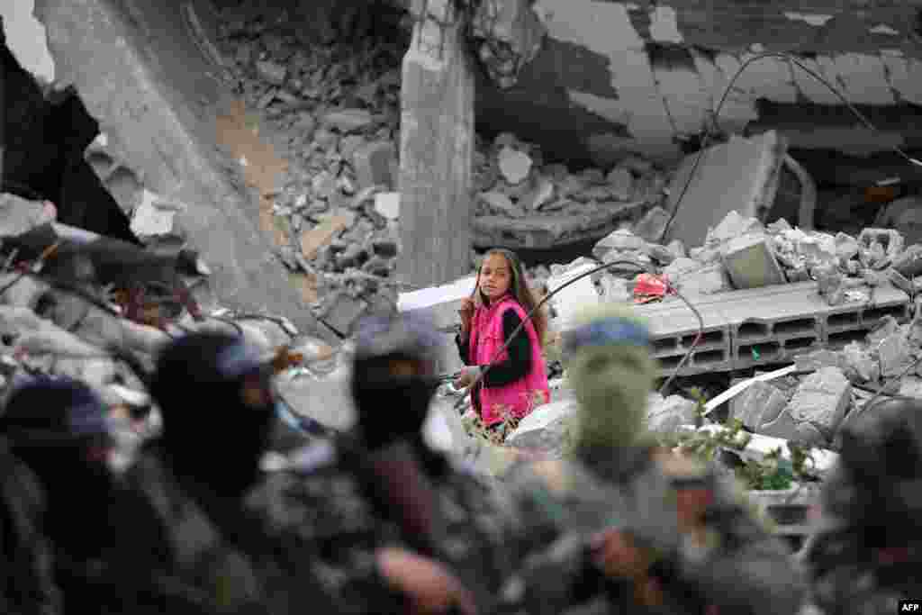 A child walks amid the rubble of a building as Palestinian fighters from the armed wing of Hamas take part in the funeral procession of Marwan Issa, a top Hamas commander killed in March 2024, in the war-devastated Bureij refugee camp in the central Gaza Strip.