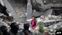 A child walks amid the wreckage of a building as Palestinian fighters from the armed wing of Hamas take part in the funeral procession of Marwan Issa, a top Hamas commander killed in March 2024, in the war-devastated Bureij refugee camp in the central Gaza Strip.