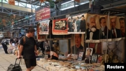 FILE - A man walks past a sign warning against the sale of illegal publications, underneath which secondhand books, images and statues of Chinese leaders are displayed for sale at the Panjiayuan antique market in Beijing, Aug. 3, 2024. 