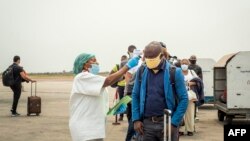 Portant des masques protecteurs pour le nez et la bouche, un employé de l'équipe d'intervention prend la température des passagers à débarquer d'un vol d'Ethiopian Airlines à l'aéroport international de N'Djili à Kinshasa, le 15 août 2020.