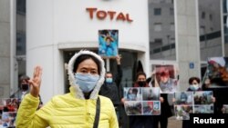 FILE - An Extinction Rebellion activist gestures in front of other activists holding pictures of Myanmar's military coup victims during a protest in front of Total headquarters, in La Defense business district, near Paris, France, March 25, 2021. 