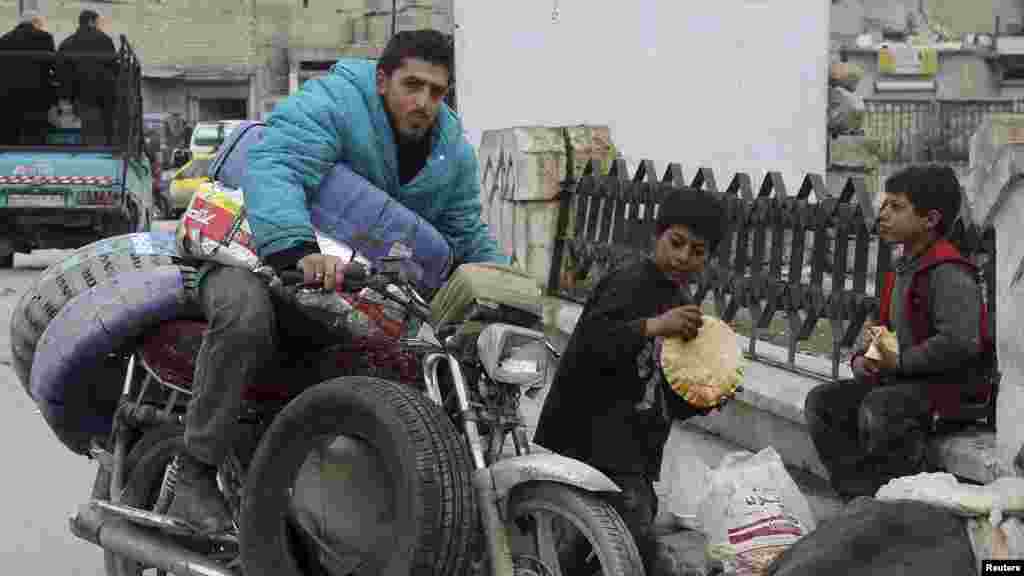 Children eat bread next to a man on a motorcycle along a street in Salehin neighbourhood in Aleppo January 25, 2014.