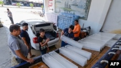 Seorang karyawan pabrik es di kota Mosul, membantu pelanggannya mengangkat dan memasukkan balok es ke dalam mobil di tengah pemadaman listrik dan suhu panas yang melanda kota tersebut, 3 JUli 2021. (AFP)
