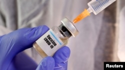 A woman holds a small bottle labbeled with a "Vaccine COVID-19" sticker and a medical syringe in this illustration taken April 10, 2020.