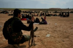 FILE - A member of the U.S.-backed Syrian Democratic Forces watches over people who were evacuated out of the last territory held by Islamic State militants, outside Baghouz, Syria, March 5, 2019.