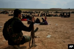 FILE - A member of the U.S.-backed Syrian Democratic Forces watches over people who were evacuated out of the last territory held by Islamic State militants, outside Baghouz, Syria, March 5, 2019.