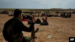 FILE -- A member of U.S.-backed Syrian Democratic Forces (SDF) watches over people who were evacuated out of the last territory held by Islamic State militants, outside Baghouz, Syria, March 5, 2019.