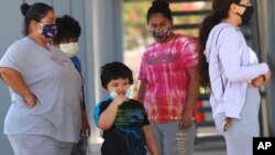 FILE - A family waits in line to check in for free COVID-19 tests at a Parkland Hospital mobile walk-up site in the Red Bird section of south Dallas, July 10, 2020. Texas again set a record for confirmed new COVID cases July 15 with nearly 10,800. 