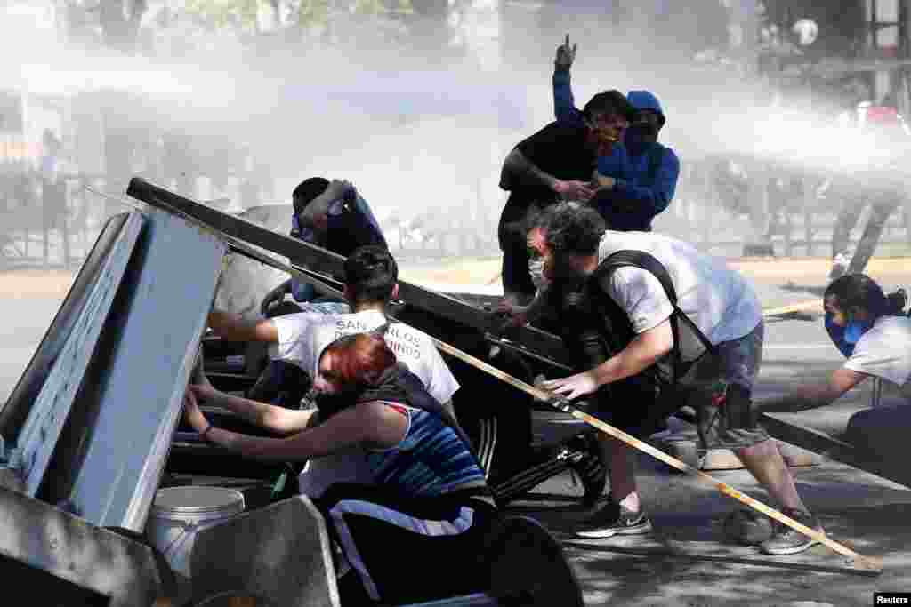 Los manifestantes se protegen de un cañón de agua de la policía detrás de una barricada durante la manifestación contra el modelo económico estatal de Chile en Santiago el 21 de octubre de 2019. REUTERS / Edgard Garrido.