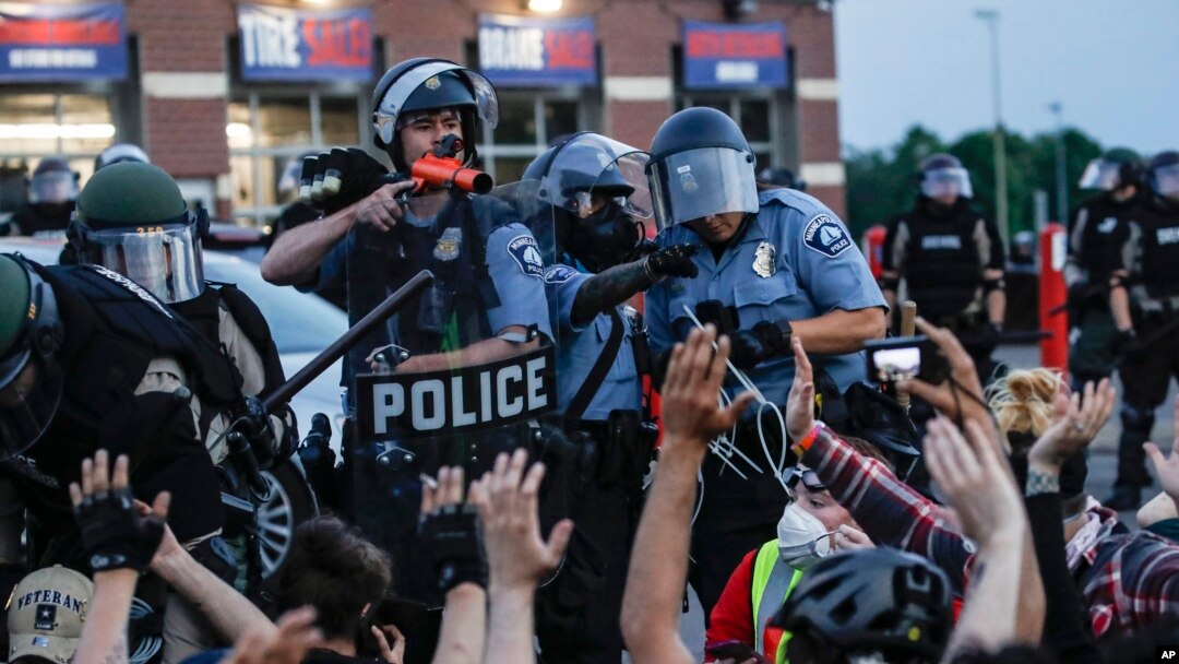 Seorang polisi mengarahkan meriam tangan ke arah demonstran yang telah ditahan sambil menunggu penangkapan di Minneapolis, 31 Mei 2020.