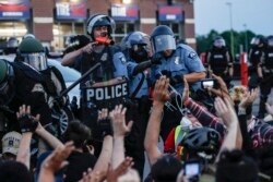 A police officer points a hand cannon at protesters who were detained pending arrest on South Washington Street, May 31, 2020, in Minneapolis.