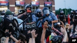 A police officer points a hand cannon at protesters who have been detained pending arrest on South Washington Street, May 31, 2020, in Minneapolis. 