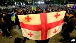 Seorang pengunjuk rasa memegang bendera Georgia selama protes oposisi terhadap hasil pemilu parlemen di Tbilisi, Georgia, Senin, 28 Oktober 2024. (Foto: AP/Shakh Aivazov)