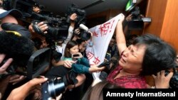 A Chinese relative of passengers aboard a missing Malaysia Airlines plane cries as she holds a banner in front of journalists reading 'We are against the Malaysian government for hiding the truth and delaying the rescue. Release our families unconditionally!" at a hotel in Sepang, Malaysia, Mar. 19, 2014.