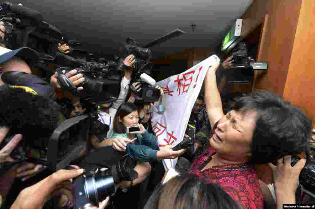 زنی که بستگانش مسافر پرواز شماره 370 خطوط هوایی مالزی بودند، در حال گریستن پرچمی را در برابر خبرنگاران تکان می دهد که روی آن نوشته شده &laquo;دولت مالزی حقیقت را از ما پنهان کرده و در نجات آنان تعلل می کند. اقوام ما را بی قید و شرط آزاد کنید!&raquo; - پکن،&nbsp; ۱۹ مارس ۲۰۱۴