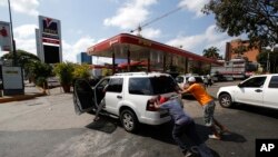 La gente empuja un automóvil sin gas a una de las pocas estaciones de combustible que tiene su propio generador eléctrico durante un apagón eléctrico en Caracas, Venezuela. Foto de archivo.