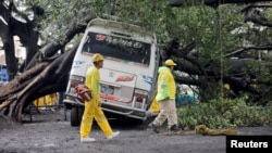 Los trabajadores de rescate caminan junto a un árbol que cayó sobre una unidad de transporte público debido a las fuertes lluvias en San Salvador, El Salvador, el 20 de junio de 2024.