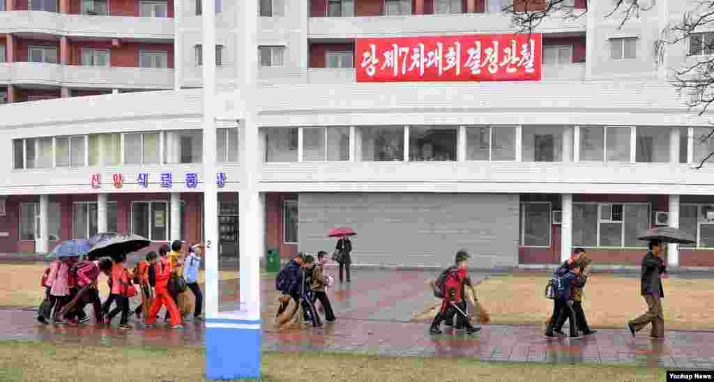 우산을 든 평양 주민들이 식료품점 앞 거리를 걷고 있다.