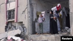 2024年2月27日，在加沙走廊南部的拉法，一名巴勒斯坦婦女抱著她的孩子，站在以色列襲擊中受損的房屋前。（路透社照片）