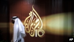FILE - A Qatari employee of the Al Jazeera Arabic language TV news channel passes by the logo of Al Jazeera in Doha, Qatar.