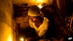 FILE - Dieusel Gerlin, a"bayakou," or waste cleaner, uses candles for illumination before descending into the pit of an outhouse in Port-au-Prince, Haiti, Dec. 22, 2016. 