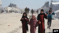 Gadis-gadis Palestina berjalan melewati puing-puing bangunan dan tenda-tenda pengungsian di kamp darurat di sebelah barat kota Jabalia di Jalur Gaza utara, 11 Maret 2025.