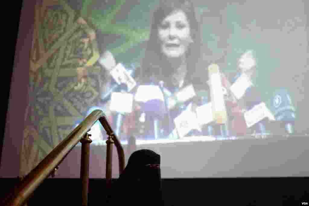 A woman in a niqab sits below a projected image of one of the conference speakers. (Y. Weeks/VOA)