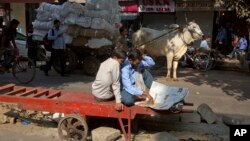 Daily wage laborers read a newspaper siting on their handcart at a market in New Delhi.