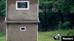 FILE - A North Korean soldier uses binoculars inside a guard tower as a woman works on a grassland on the banks of Yalu River, near the North Korean town of Sinuiju, opposite the Chinese border city of Dandong, June 12, 2013. 