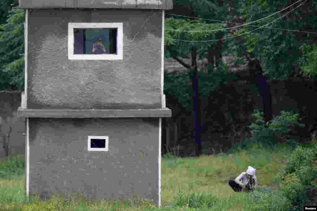 A North Korean soldier uses binoculars inside a guard tower as a woman works on a grassland on the banks of Yalu River, near the North Korean town of Sinuiju, opposite the Chinese border city of Dandong.