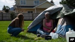 Cassy Leach, enfermera que dirige un grupo de voluntarios que dan alimentos, atención médica y bienes básicos a cientos de personas sin hogar en los parques, habla con Kimberly Marie, que acampa en Fruitdale Park, el 21 de marzo de 2024, Grants Pass, Oregon, EEUU.