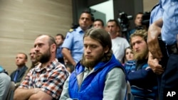Kosovo police officers stand guard next to, from left, Kenan Plakaj, Arton Ahmeti, center, and Leotrim Musliu, second row right, in court for the foiled attack against the Israeli team in a 2016 qualifying World Cup match in neighboring Albania, in Kosovo's capital Pristina, May 18, 2018.